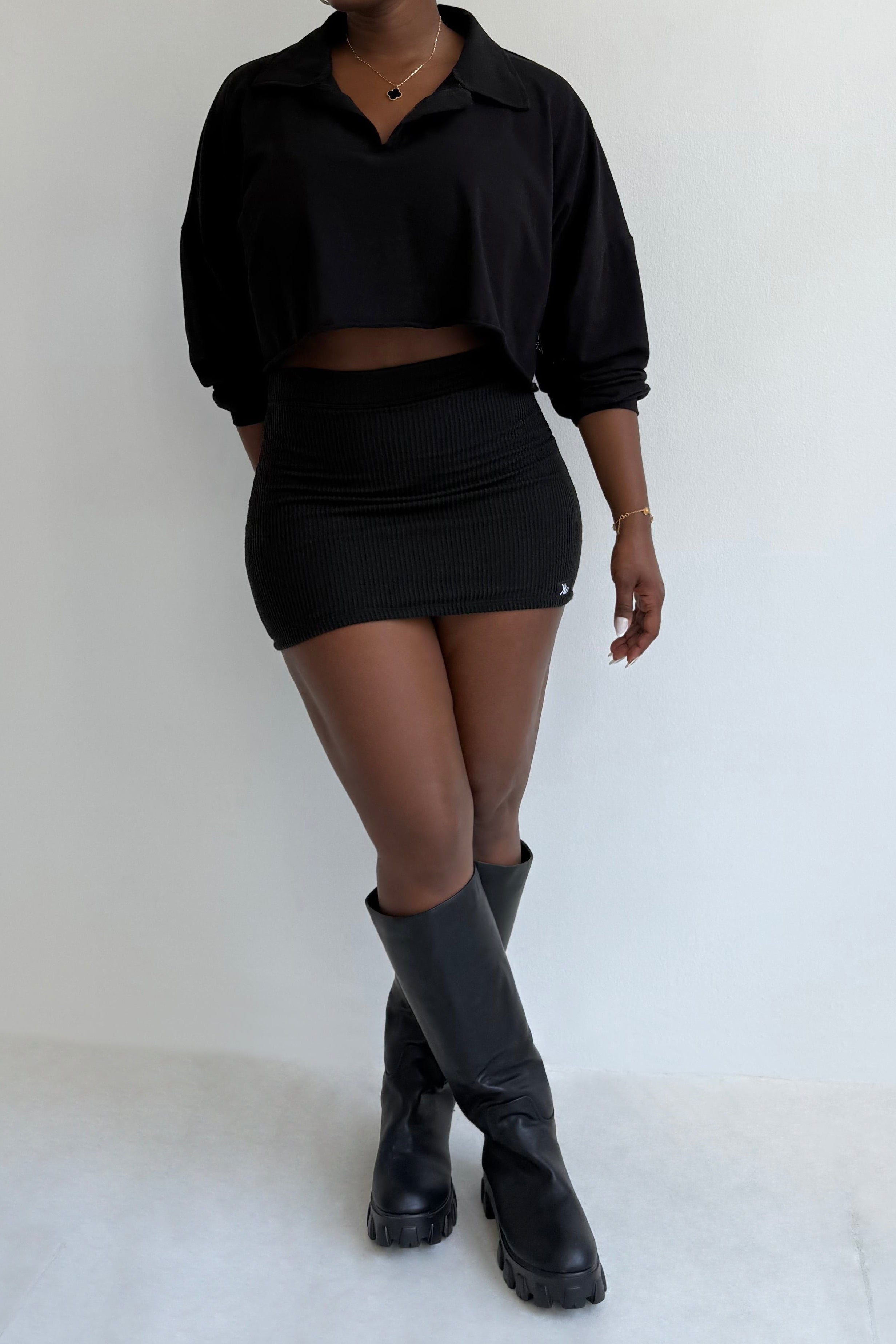 Person wearing a black outfit with knee-high boots on a white background